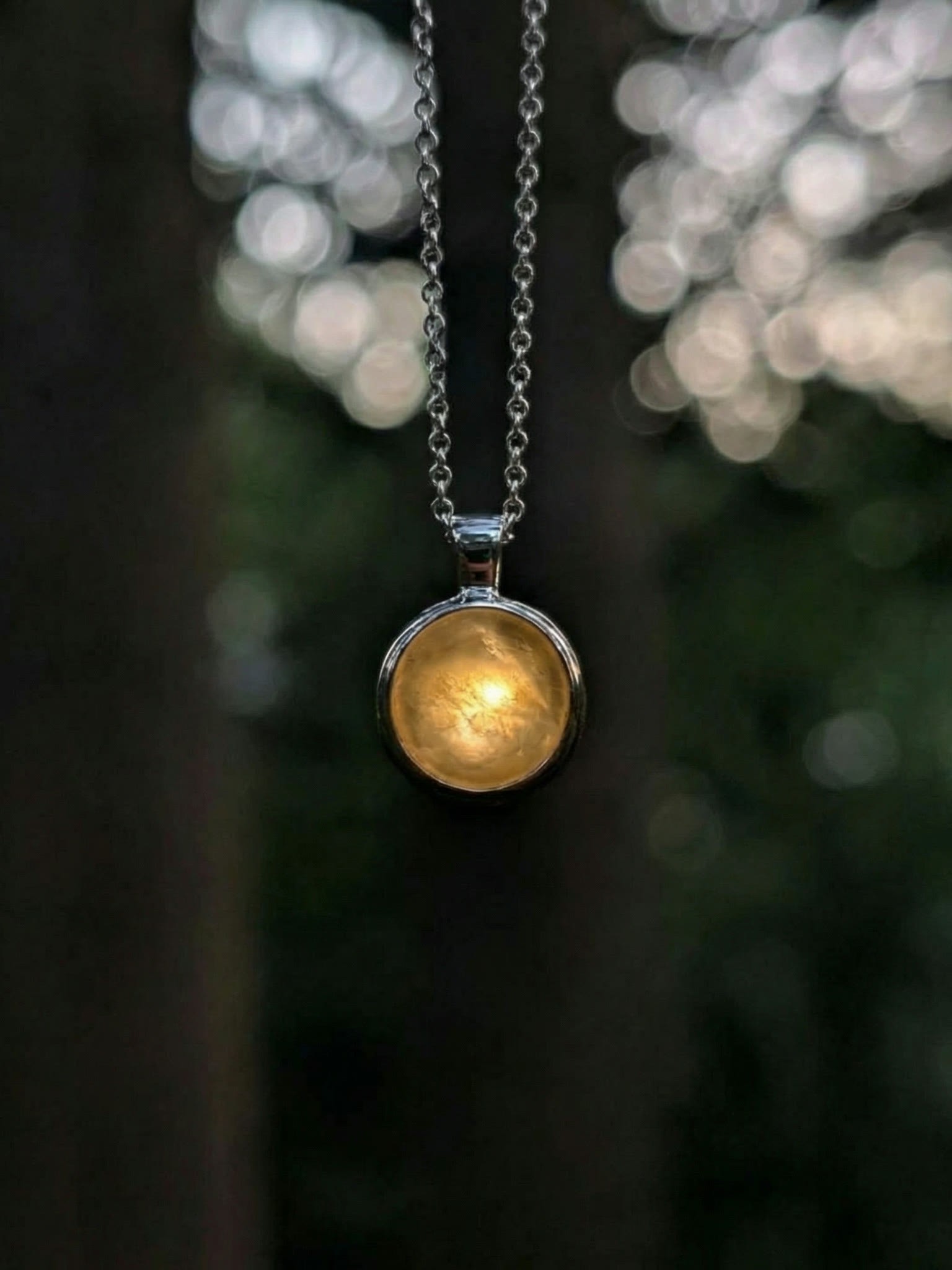 Louis Jacques self-illuminating sterling silver necklace glowing in close-up against bokeh woodland background.