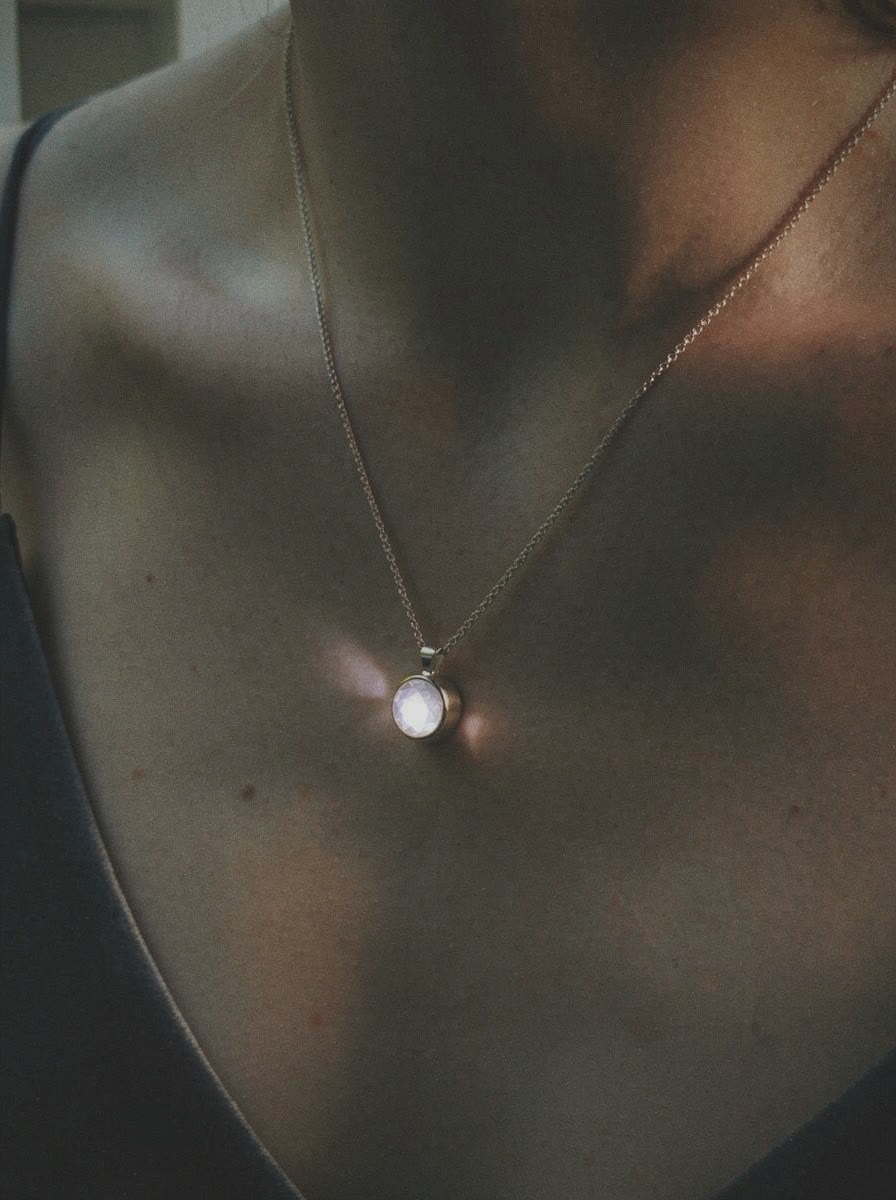 Close-up of Louis Jacques pendant on chest, stone casting a soft light on skin