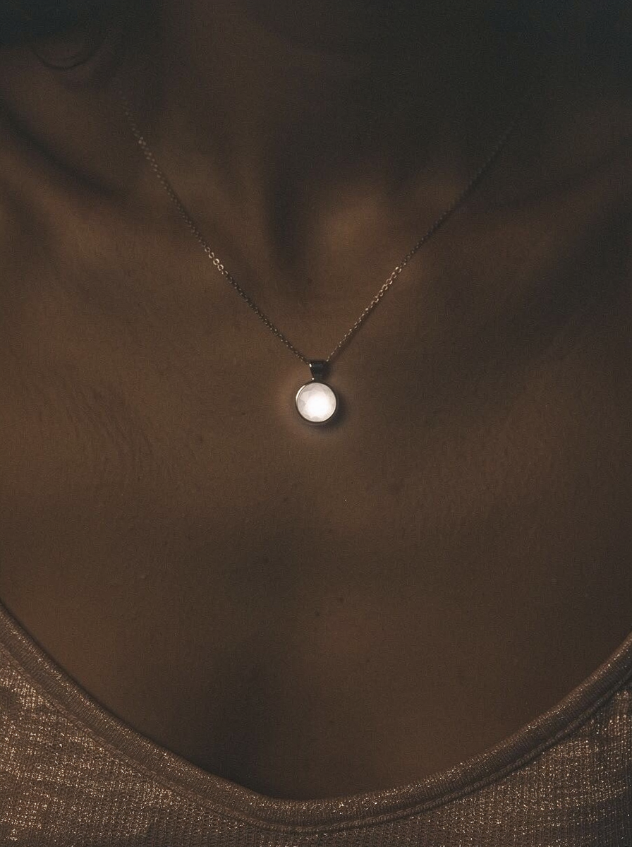 Woman in dark, moody lighting with Louis Jacques pendant glowing softly at her neckline